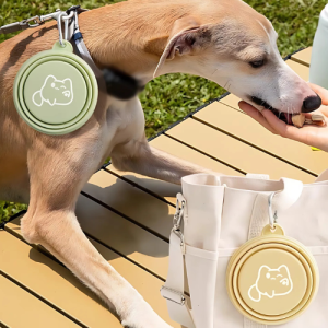 Sammenleggbar Matskål og Vannskål for Hund – Lett og Praktisk Design for Tur og Utendørs Eventyr Hund spiser godbit ute med grønt bånd og grønn slikkebolle; beige sammenleggbar skål henger på hvit veske.